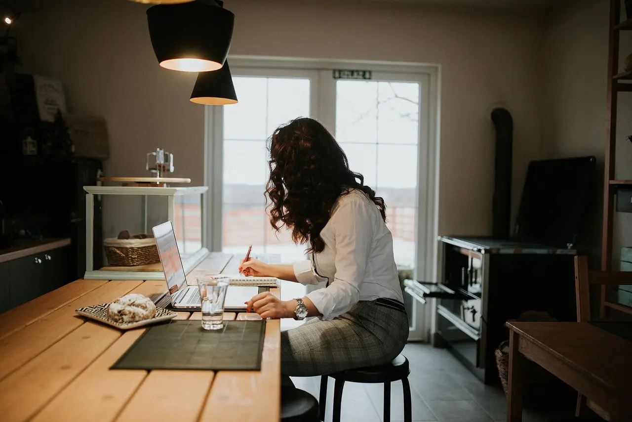 Mujer trabajando en su notebook y tomando notas en una cocina luminosa.